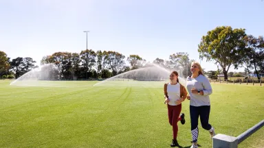 Two women jogging around sports oval that is being watered by recycled water