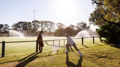 Two women stretching at a sports oval that is being watered with recycled water